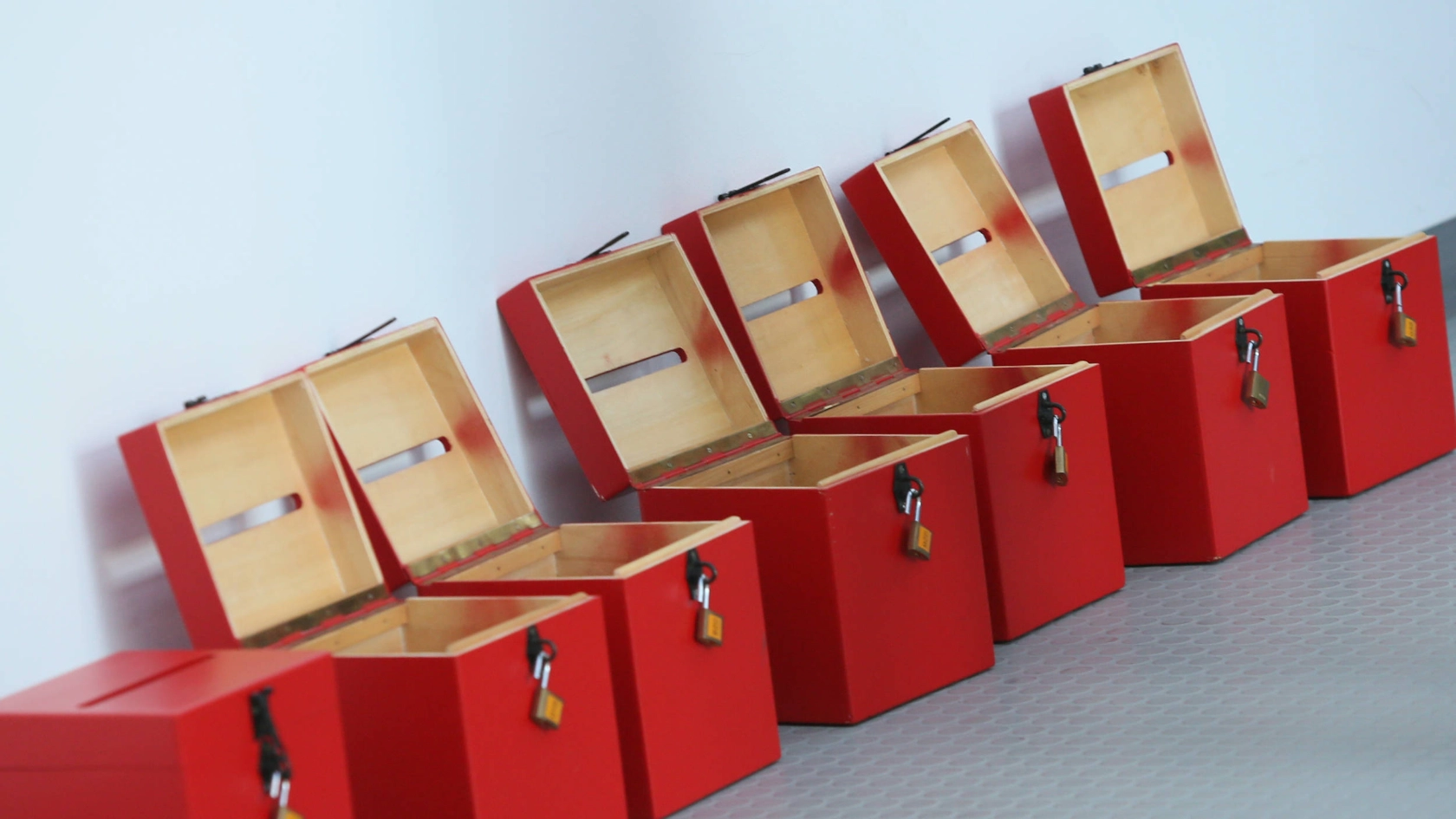 Offene Wahlurnen in rot stehen vor einer weißen Wand.