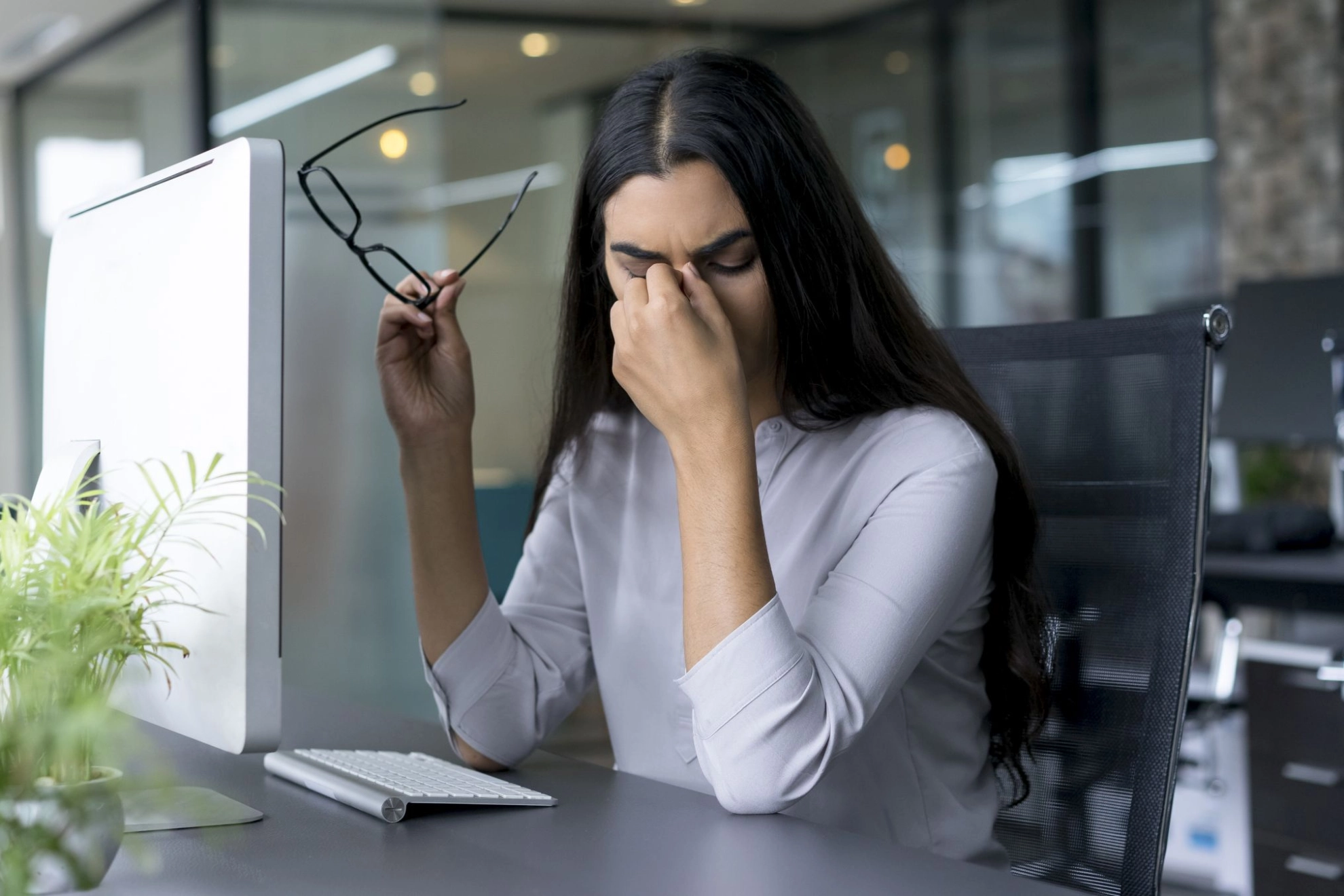 Eine junge Frau reibt sich im Büro aus Übermüdung die Augen