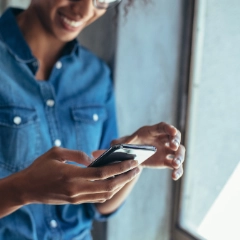 Eine junge Frau schaut lächelnd auf ihr Handy.